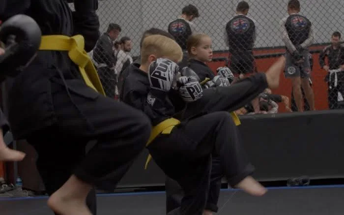 Young Junior Warriors in uniform and gloves drilling knee strikes and kicks
