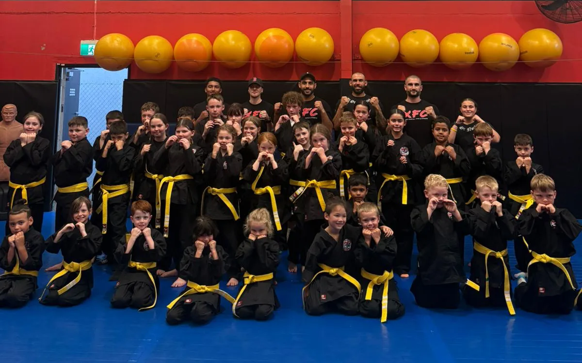 The junior class in uniform with their yellow belts, fists up alongside the XFC coaching team